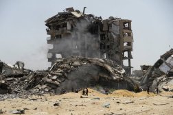 فلسطينيون يسيرون بجوار أنقاض مبان دمرتها الغارات الإسرائيلية (رويترز)